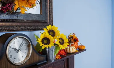 a mantel above a fireplace with a clock, sunflowers and miniature pumpkins