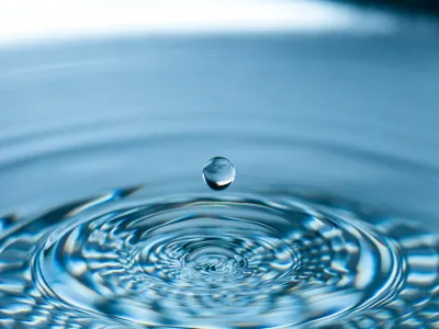 Close-up of a water droplet falling and creating ripples on a calm blue surface.