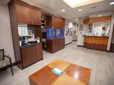 Waiting room with wooden furniture, fish tank, coffee station, and reception desk in a professional office.