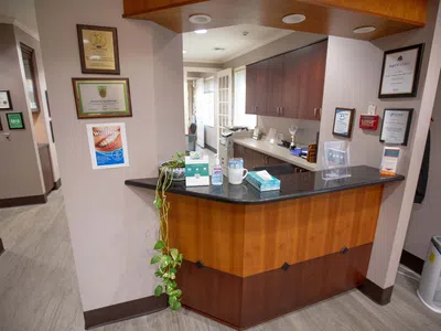 Reception desk area with wood paneling, granite countertop, certificates on beige walls, and office supplies in dental clinic.