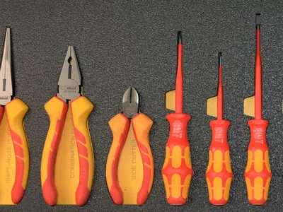 Set of insulated hand tools including pliers and screwdrivers with yellow and red handles on a dark background