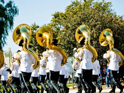 Marching band in white uniforms playing sousaphones outdoors during a sunny parade or event.