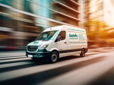 White delivery van for Lapels Laundromat driving fast on city street during sunset with blurred background.