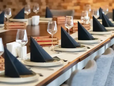 Elegant dining table set with black napkins, white plates, wine glasses, and gray cushioned chairs in a modern restaurant.
