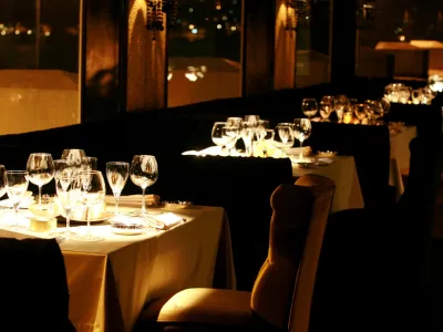 Elegant restaurant dining tables set with wine glasses and candles in warm, ambient evening lighting.