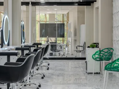 Modern salon interior with black styling chairs, illuminated circular mirrors, and green decorative chairs on marble floor.