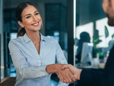 Smiling woman shaking hands with man in office setting during a professional meeting or interview.