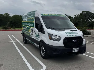 White delivery van with laundromat branding parked in an empty lot under cloudy sky.