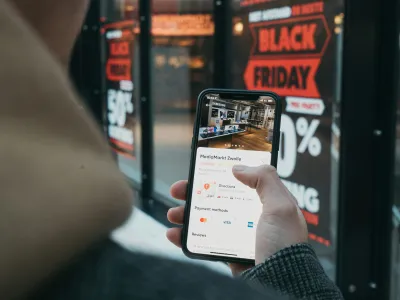 Person holding smartphone displaying MediaMarkt Zwolle app with Black Friday sale signs in background
