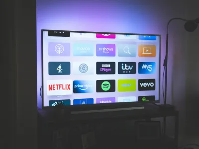 Smart TV screen displaying streaming apps like Netflix, Prime Video, Spotify, and BBC iPlayer in a dimly lit room.