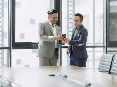 Two business professionals discussing over a smartphone in a modern office setting.
