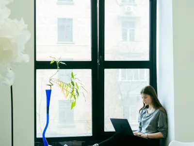 a woman sitting on a couch with a laptop in front of a window