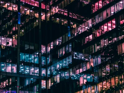 Night view of a modern office building with colorful illuminated windows and reflections on glass facade.