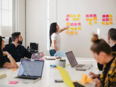 Team collaborating in a bright office with sticky notes on the wall and laptops open around a white table.