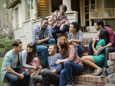 Group of young adults socializing and laughing together on a house porch steps on a sunny day