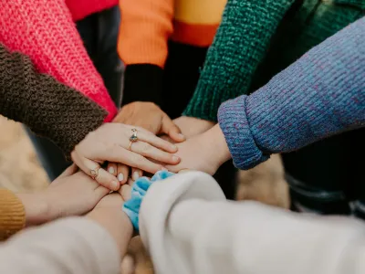 Group of people putting hands together in a show of unity and teamwork with colorful sweaters.