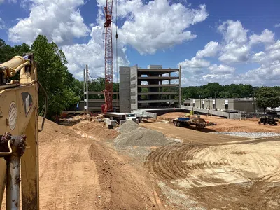Active construction site with a crane, excavator, and multi-story concrete building under development on a sunny day.
