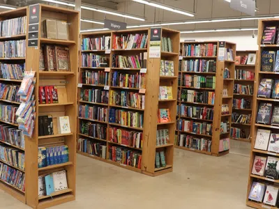 Interior view of a library with wooden bookshelves filled with books under bright fluorescent lights