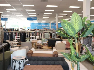 Furniture, decor, and clothing racks arranged in a bright department store interior under fluorescent lights.