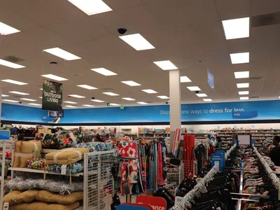 Interior view of a retail store showing clothing racks and colorful cushions under bright ceiling lights.