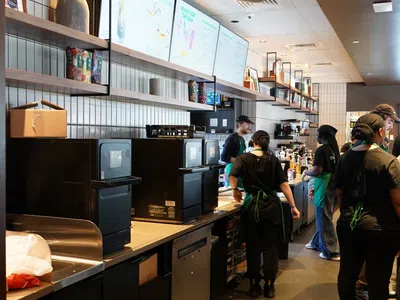 Busy coffee shop counter with staff preparing drinks and digital menu boards overhead