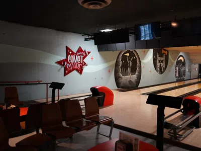 Interior view of a retro bowling alley with wooden seats, lanes, and vintage wall art at Comet Spare.