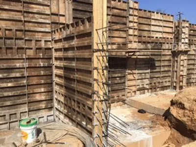Wooden concrete formwork panels installed with rebar rods at a construction site under clear sky.