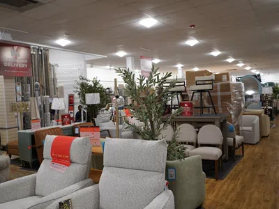 Furniture store interior with sofas, chairs, lamps, and home decor items displayed on wooden flooring under bright ceiling lights.