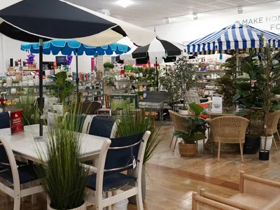 Indoor furniture store display featuring patio tables with umbrellas, chairs, and potted plants on wooden floor.