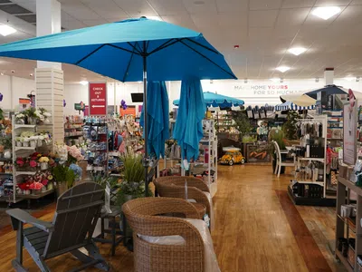 Indoor view of a home goods store featuring wicker chairs, blue umbrellas, and various decorative items on display.