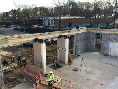 Construction site with workers, scaffolding, concrete pillars, and steel beams under clear daylight conditions.