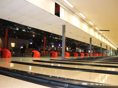 Empty bowling alley lanes with red seating and dimly lit interior under a bright ceiling.
