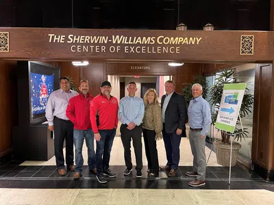 Group of seven professionals standing under Sherwin-Williams Company Center of Excellence sign inside office building.