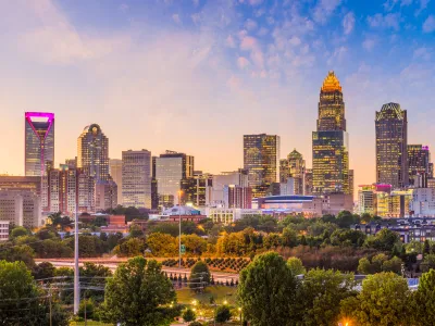 Charlotte skyline at sunset with illuminated skyscrapers and lush green park in foreground under a colorful sky