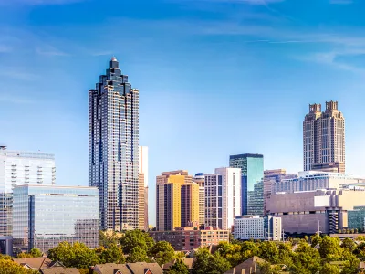 Panoramic view of a city skyline with modern skyscrapers and green trees under a clear blue sky.