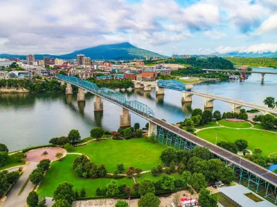 Aerial view of a city with two bridges crossing a river, green parks, and a mountain in the background under a cloudy sky