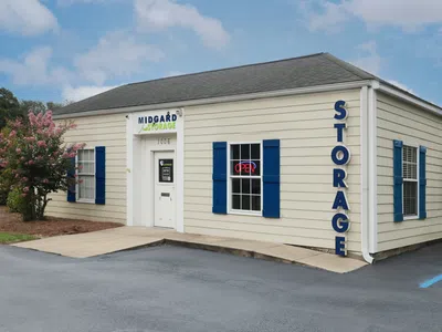 Midgard Storage facility building with beige siding, blue shutters, and an open neon sign on a clear day