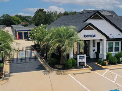 Self storage facility with gated entrance, white office building, palm trees, and outdoor parking spaces on sunny day