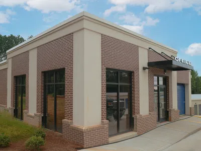 Small brick and beige commercial office building with glass windows and black awning on entrance.