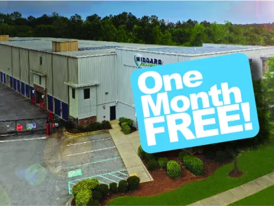 Industrial storage facility with parking lot and signage offering one month free promotion on a clear sunny day.