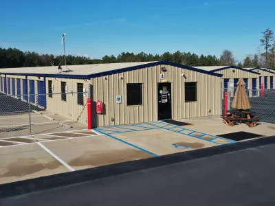 Outdoor self-storage facility with multiple beige metal units and a small office building under clear blue sky.
