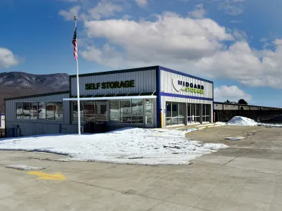 Self storage facility with snow-covered ground, clear blue sky, and American flag on a pole outside the building.