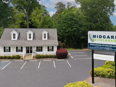 White office building of Midgard Self Storage with empty parking lot and large business sign in front.