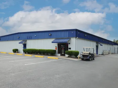 Large industrial warehouse with white walls and blue roof under a partly cloudy sky with an empty parking lot