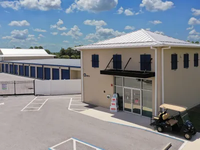 Modern storage facility with blue roll-up doors, office building, golf cart, and clear blue sky.