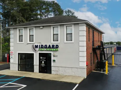 Midgard Self Storage facility with office building, parking spaces, and outdoor storage units under blue sky.