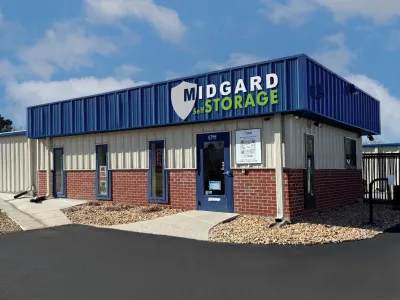 Midgard Self Storage facility with blue and beige exterior, brick lower walls, and clear signage under a blue sky.