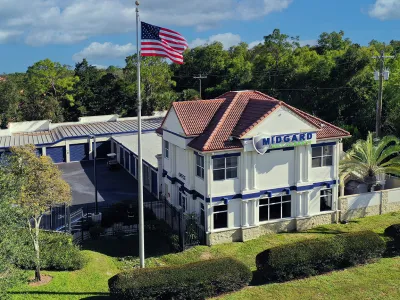 Midgard Storage office with red tile roof, American flag, outdoor storage units, and greenery under a blue sky.