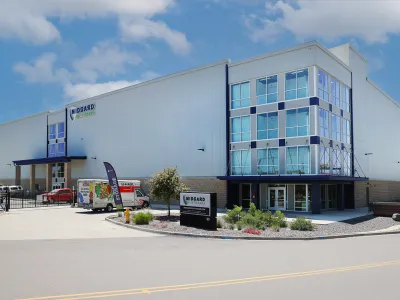 Modern industrial building with glass entrance and white metal siding under a bright blue sky
