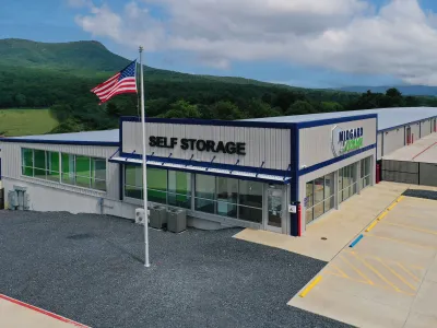 Self storage facility building with large windows, American flag, and outdoor storage units with mountain backdrop.